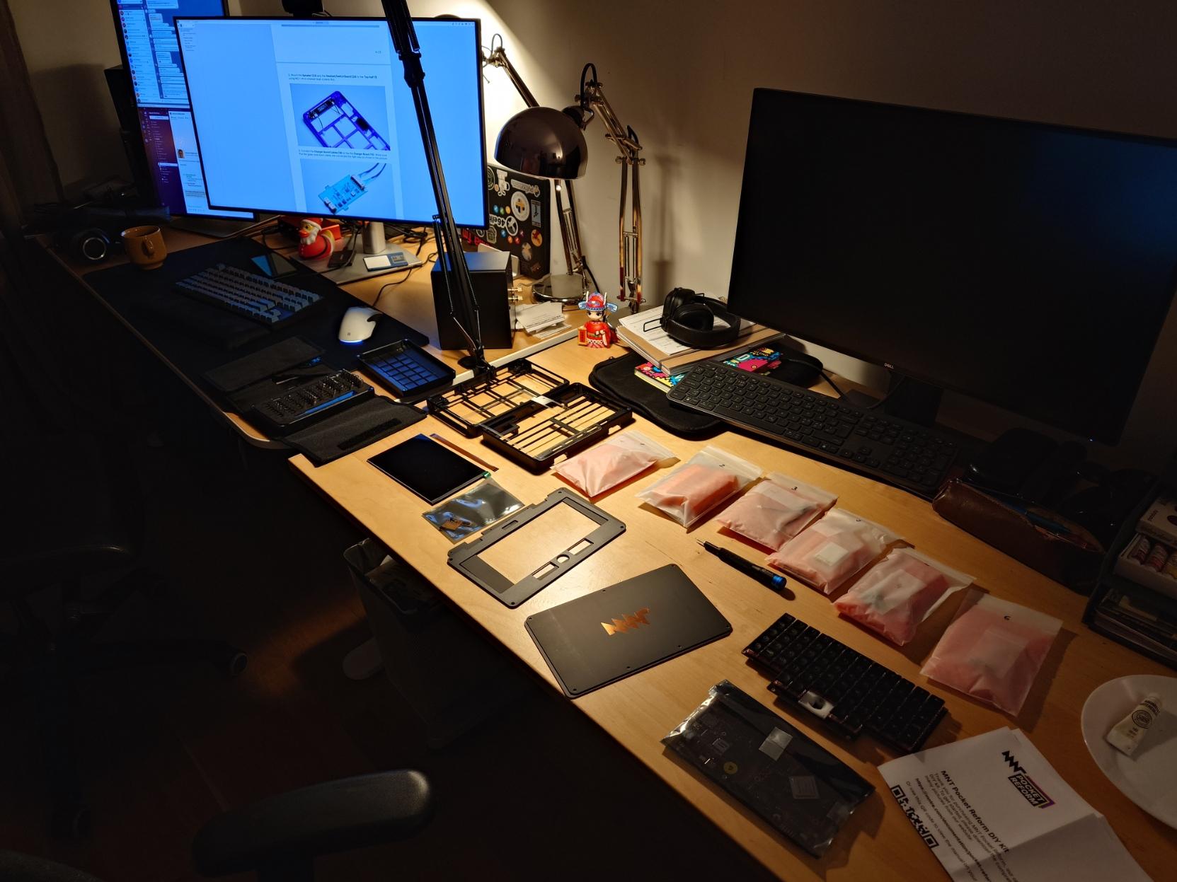 An MNT Pocket Reform DIY kit on a desk, just unpacked and ready to be assembled. Assembly manual in the background on a monitor.