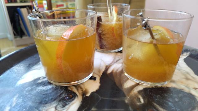 Tre gulorange drinkar med is, drinkpinnar, äppelskivor och kanelstång står på en bricka.