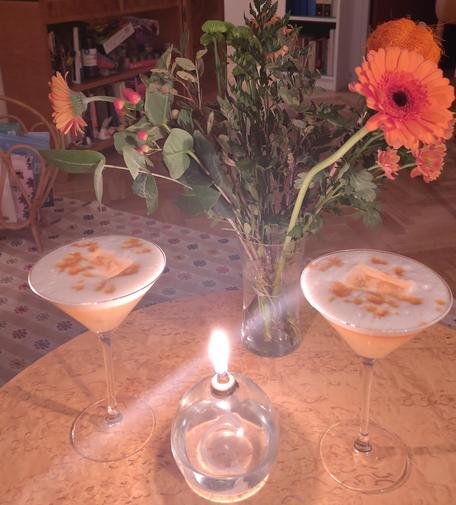 Två drinkar med orange botten och skum med orange prickar. Ett ljus och en bukett med orange blommor.