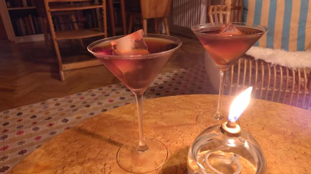 Två genomskinligt rödbruna drinkar med stora isbitar vid en tänd oljelampa.