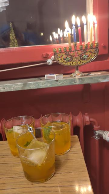 Tre gula drinkar med is, mynta och lime framför en chanikia med sex ljus.