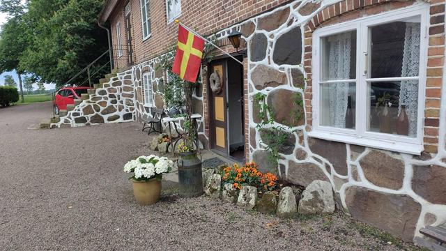 En gårdslånga i sten och tegel där en skånsk flagga hänger vid entren.