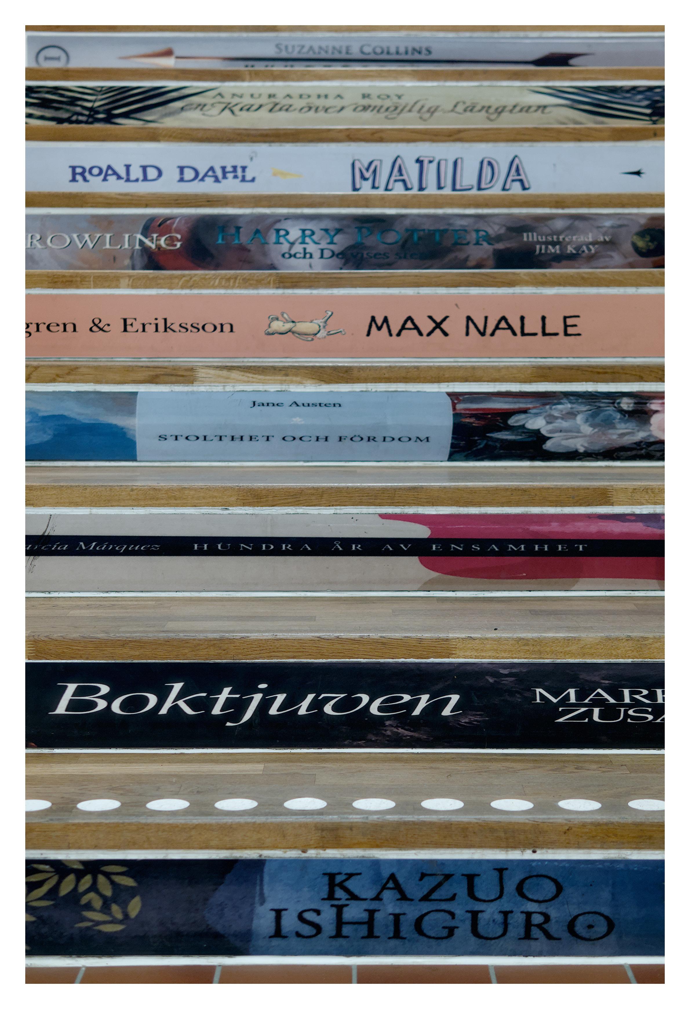 En stående bild med liggande bilder på olika bokryggar som bildar en trappa. Längst ner en liten del av golvet. Bland boktitlarna finns bland annat Matilda av Roald Dahl, en Harry Potter, en av Kazuo Ishiguro och Stolthet och fördom av Jane Austen.