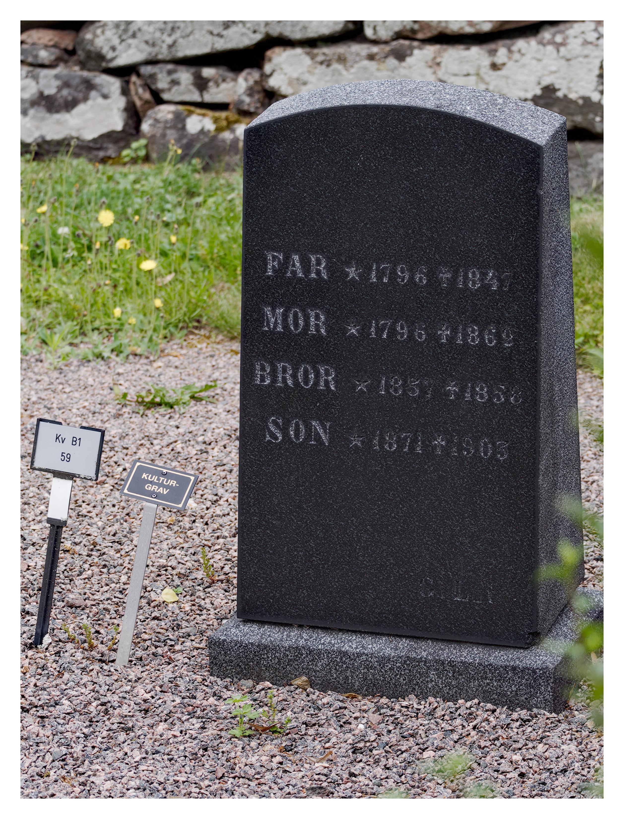 En stående bild på en mörkgrå gravsten med FAR, MOR, BROR och SON uppifrån och ner. De är födda på 1700- och 1800-talet. Grus runtom, gräs och en stenmur bakom. Bredvid sitter en liten skylt med texten "KULTURGRAV".